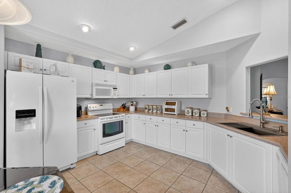 A kitchen features white cabinets, tan countertops, tile flooring, and white appliances — 39 WHEELING LANE, PALM COAST, FL