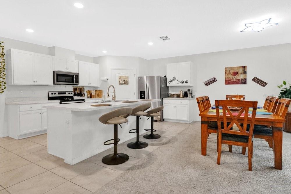 A kitchen with white cabinets, a central island with bar stools, and a dining area — 628 REINDEER DRIVE, KISSIMMEE, FL