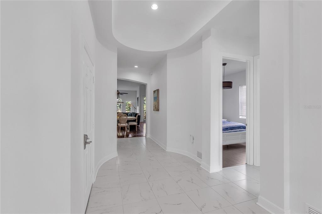 A bright hallway with white marble-look tile flooring leads toward a dining area and bedroom — 5469 46TH COURT W, BRADENTON, FL