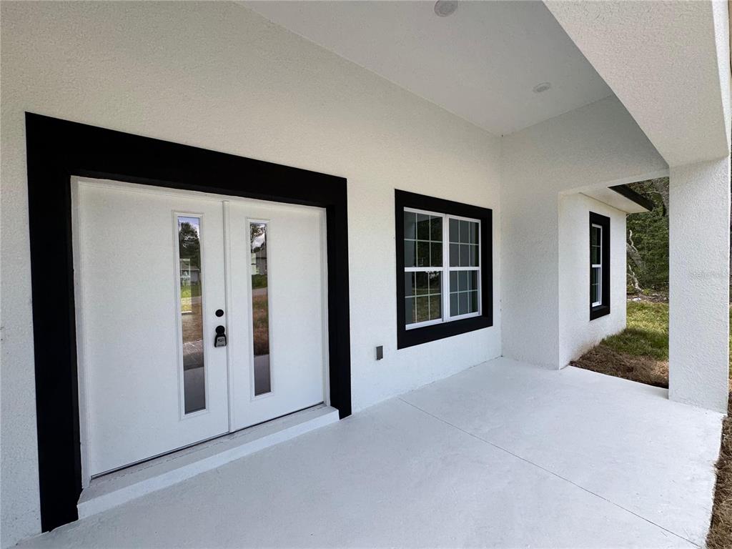 A white covered porch features a double front door and windows with black trim — 8210 N BROOK WAY, CITRUS SPRINGS, FL