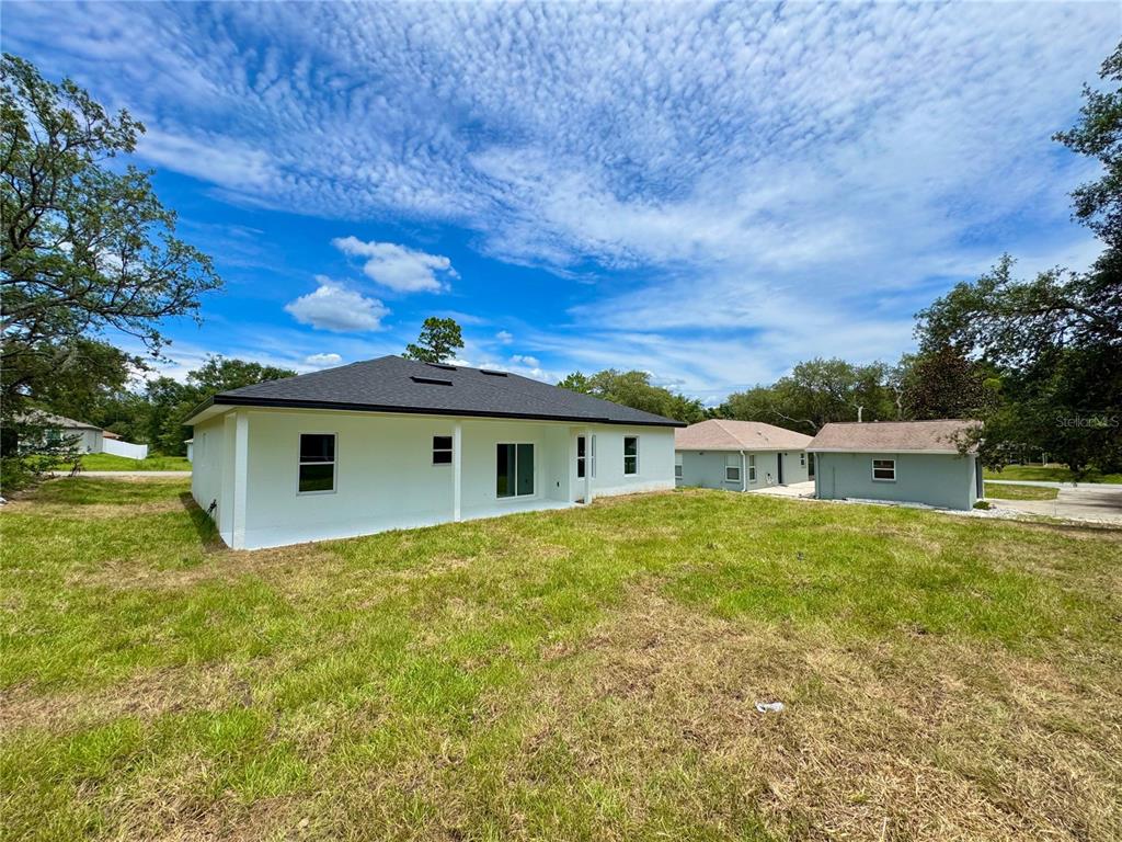 The rear exterior of a white single-story house with a black roof and grassy yard — 8210 N BROOK WAY, CITRUS SPRINGS, FL