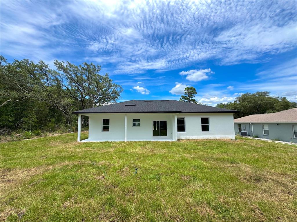 The rear exterior of a white single-story house features a covered patio and lawn — 8210 N BROOK WAY, CITRUS SPRINGS, FL