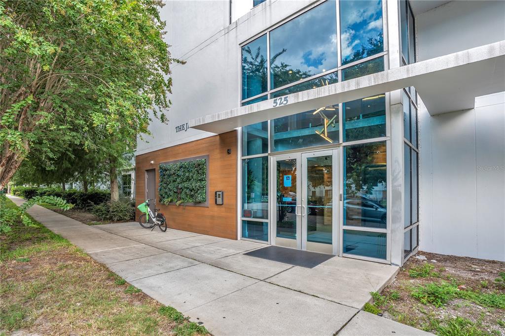 The exterior entrance of a modern building features glass doors, a wood-paneled wall, and landscaping — 525 E JACKSON STREET UNIT 509, ORLANDO, FL