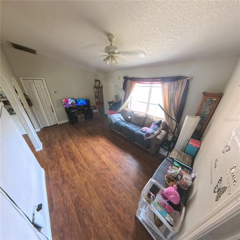 A living room with wood-look flooring, a sofa, a computer desk, and a ceiling fan — 706 N RENNES COURT, KISSIMMEE, FL