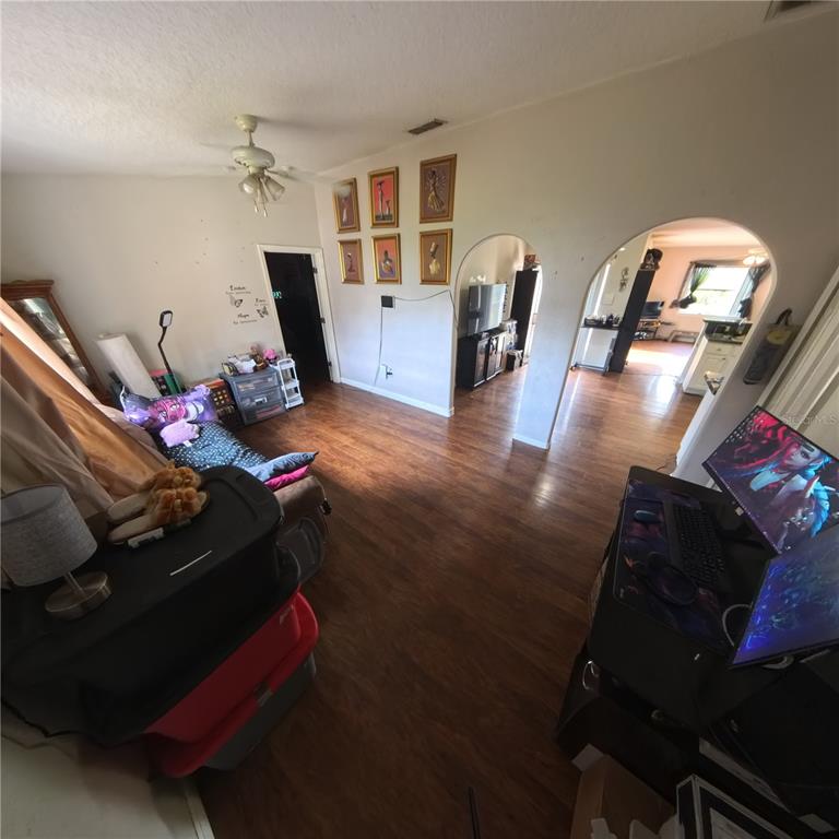 A living room with wood-look flooring, arched doorways, and a computer desk in the foreground — 706 N RENNES COURT, KISSIMMEE, FL