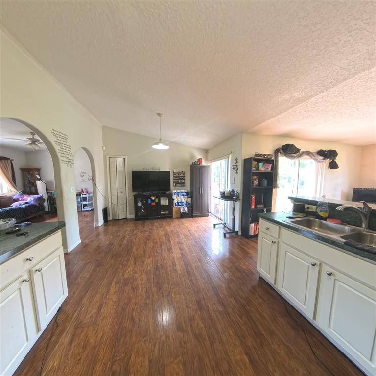 A kitchen with white cabinets and a sink overlooks an open-concept living area with wood flooring — 706 N RENNES COURT, KISSIMMEE, FL