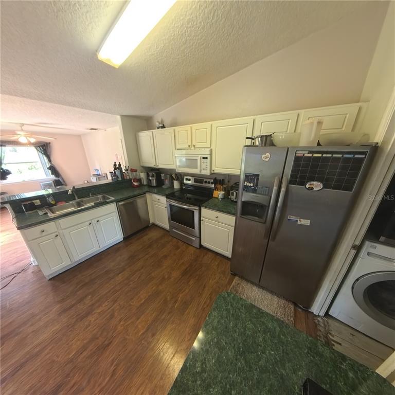 A kitchen with white cabinets, stainless steel appliances, and green countertops features wood-look flooring — 706 N RENNES COURT, KISSIMMEE, FL