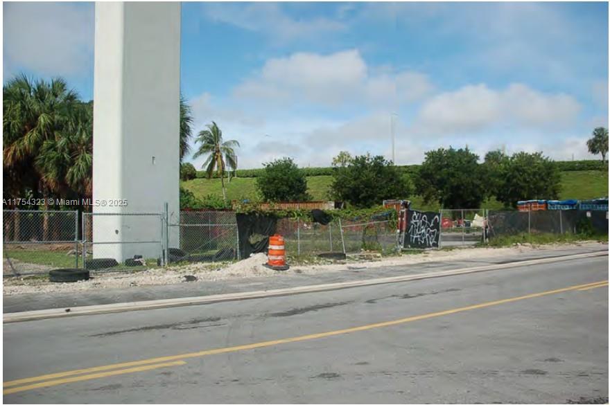 A fenced vacant lot features a large concrete pillar and a grassy embankment in the background — 3632 NW 37 Avenue, Miami FL 33142, MIAMI, FL