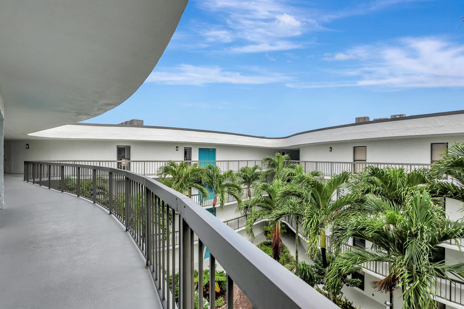 A curved outdoor walkway overlooks a multi-story apartment building courtyard filled with palm trees — 1357 NE Ocean Boulevard # 311, Stuart FL 34996, STUART, FL