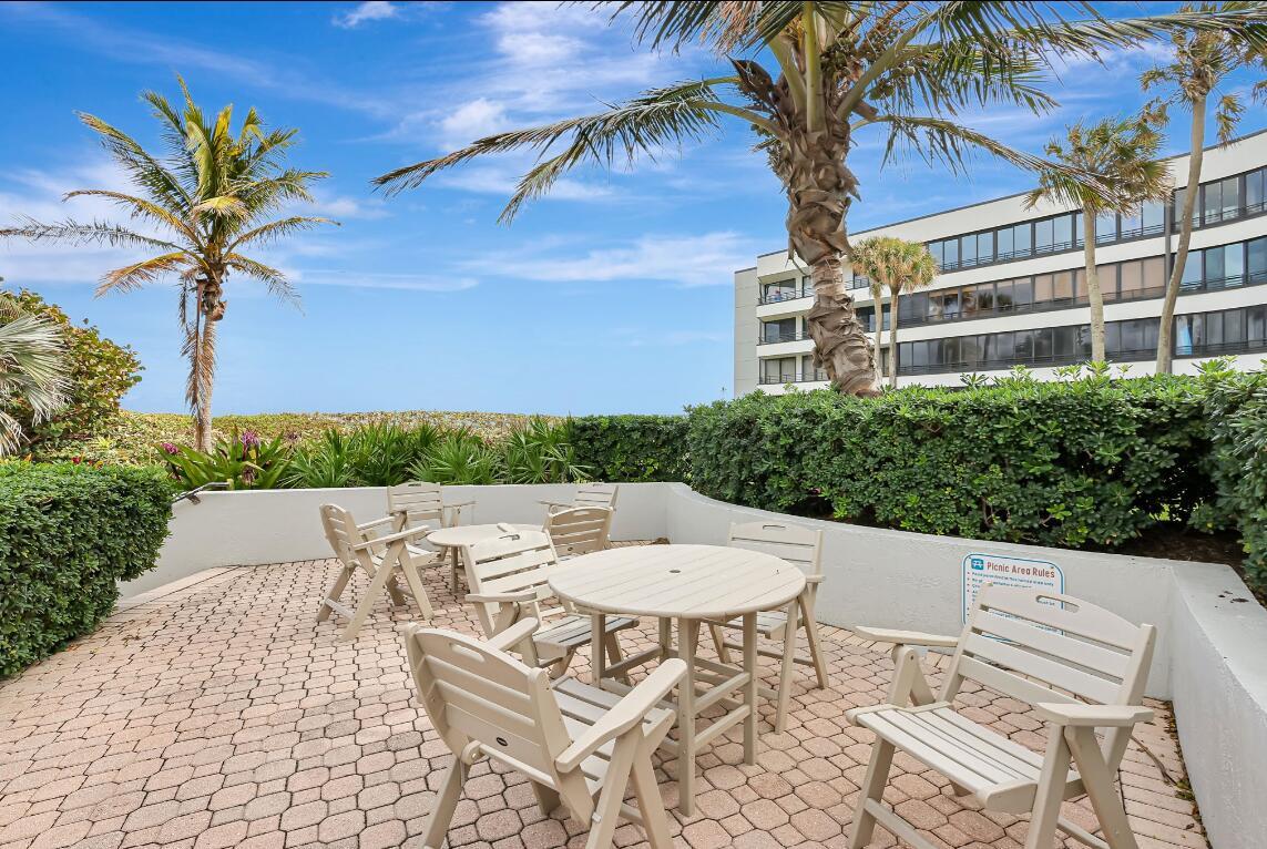 An outdoor patio with tables and chairs sits near a beach with palm trees — 1357 NE Ocean Boulevard # 311, Stuart FL 34996, STUART, FL