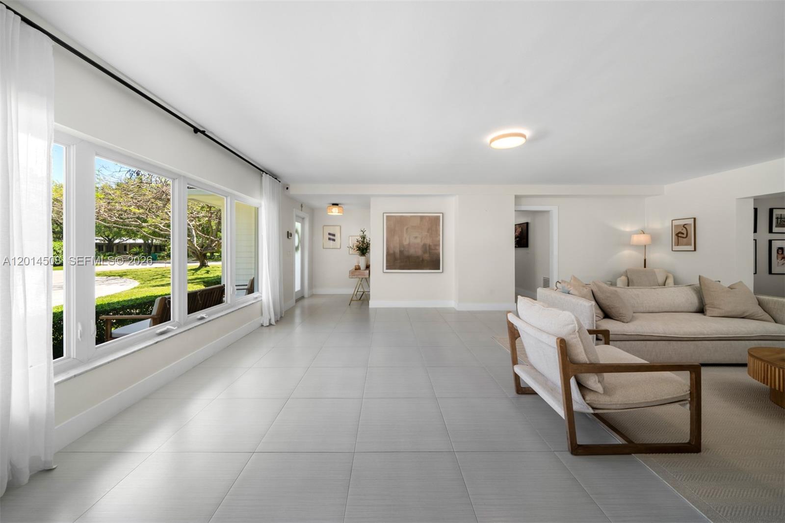 A bright living room features large windows, light tile flooring, and neutral-toned furniture — 6450 SW 128th St, Pinecrest FL 33156, PINECREST, FL