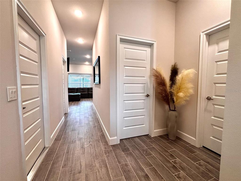 A hallway with wood-look tile flooring leads to a living area with three white doors — 11801 SUNDER BERRY STREET, HUDSON, FL