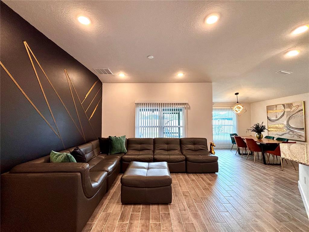 A living room with a dark accent wall, brown sectional sofa, and adjacent dining area — 11801 SUNDER BERRY STREET, HUDSON, FL