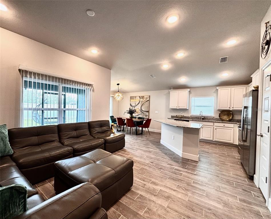 An open-concept living room and kitchen featuring dark leather furniture, white cabinetry, and tile flooring — 11801 SUNDER BERRY STREET, HUDSON, FL