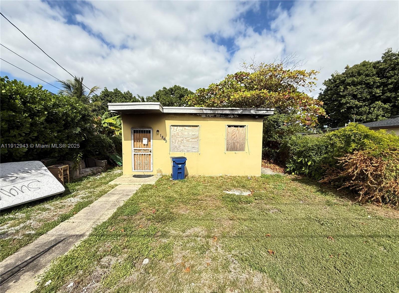 A small, single-story yellow house with boarded-up windows and a metal security screen door — 1865 NW 70th St, Miami FL 33147, MIAMI, FL