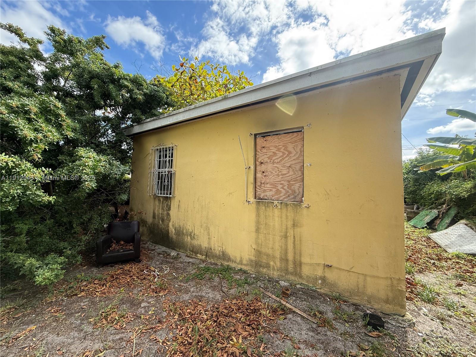 The exterior of a yellow, weathered building features a boarded-up window and a metal-grated window — 1865 NW 70th St, Miami FL 33147, MIAMI, FL