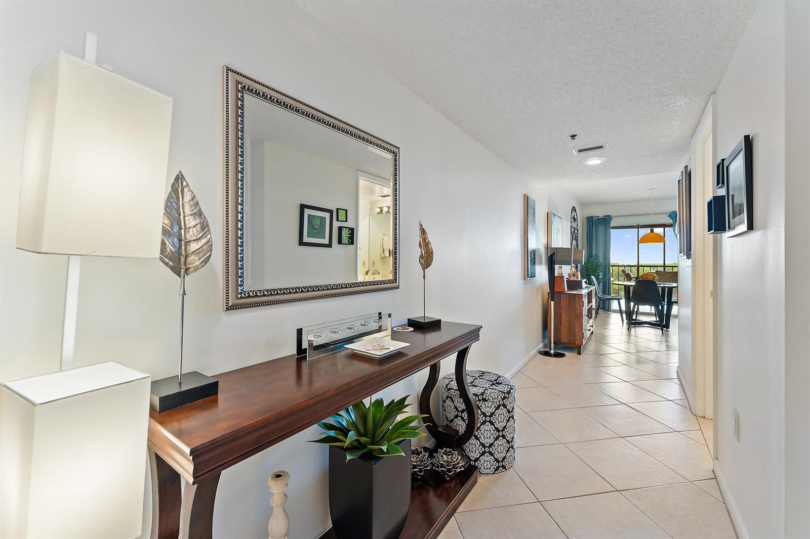 A hallway with a wooden console table, a large mirror, and tiled flooring leads to a dining area — 275 Palm Avenue # C503, Jupiter FL 33477, JUPITER, FL