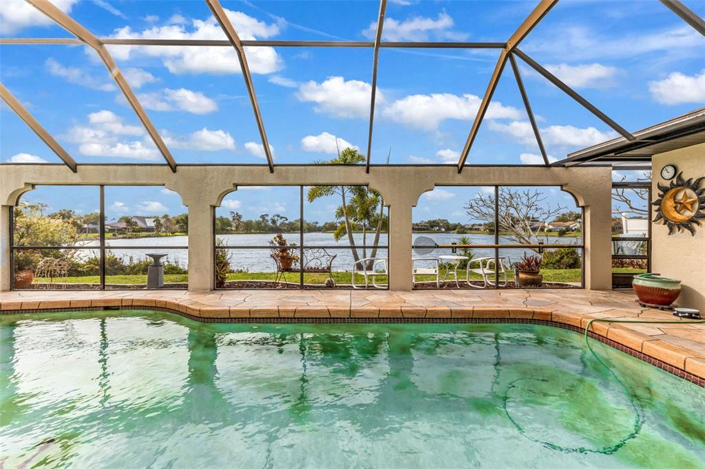 A screened-in swimming pool patio overlooks a lake with a stone-tiled deck — 23439 FREEPORT AVENUE, PORT CHARLOTTE, FL