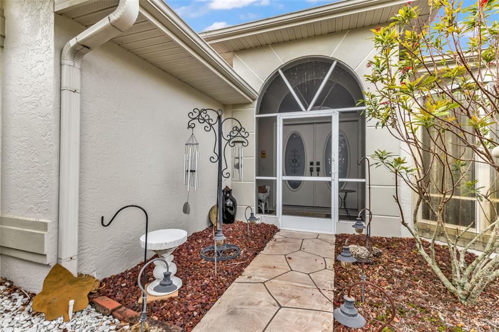 A stone walkway leads to a front entrance with a white screen door and archway — 23439 FREEPORT AVENUE, PORT CHARLOTTE, FL