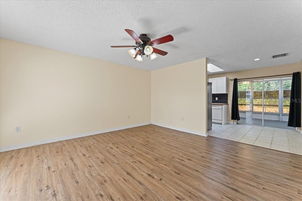 An empty living room with wood-look flooring, a ceiling fan, and an adjacent tiled kitchen — 3701 MODESTO STREET, NEW PORT RICHEY, FL