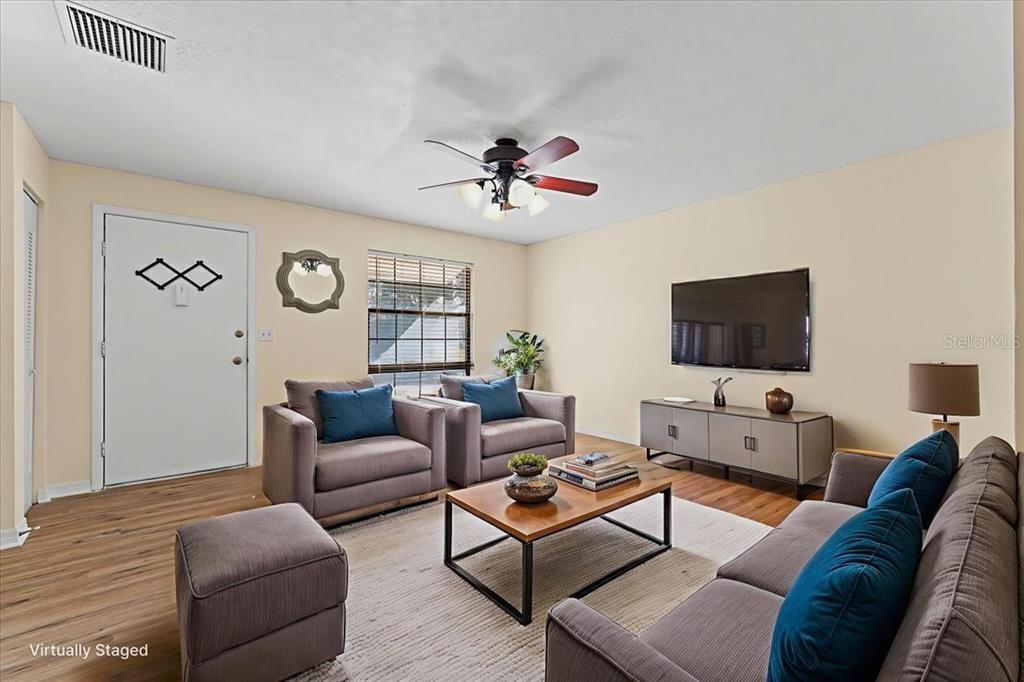 A living room features wood-look flooring, a ceiling fan, and furniture arranged around a television — 3701 MODESTO STREET, NEW PORT RICHEY, FL