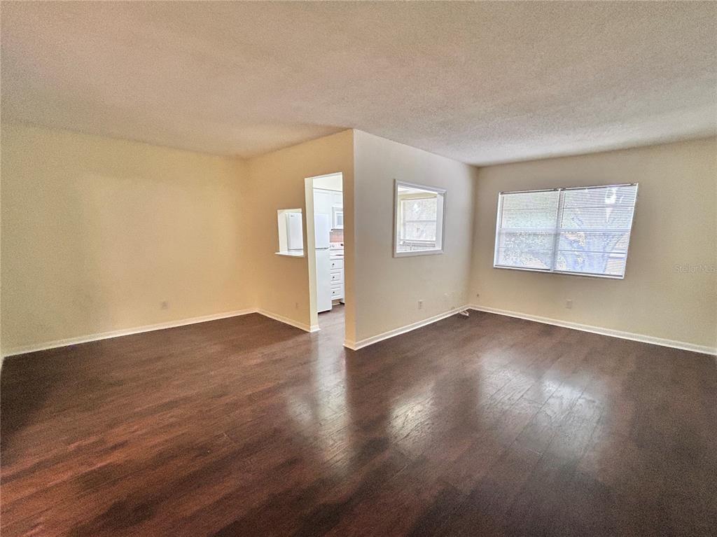 An empty living room features dark wood-look flooring, beige walls, and a pass-through kitchen window — 4455 38TH TERRACE N UNIT B16, ST PETERSBURG, FL