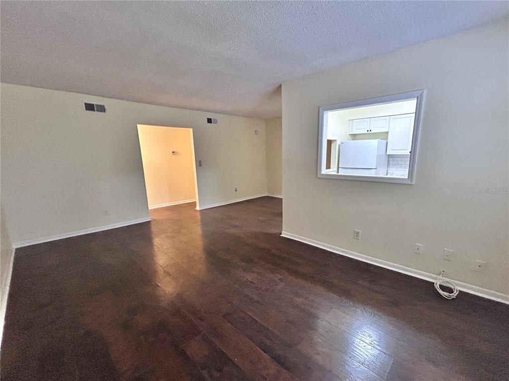An empty room with dark wood floors and a pass-through window to the kitchen — 4455 38TH TERRACE N UNIT B16, ST PETERSBURG, FL