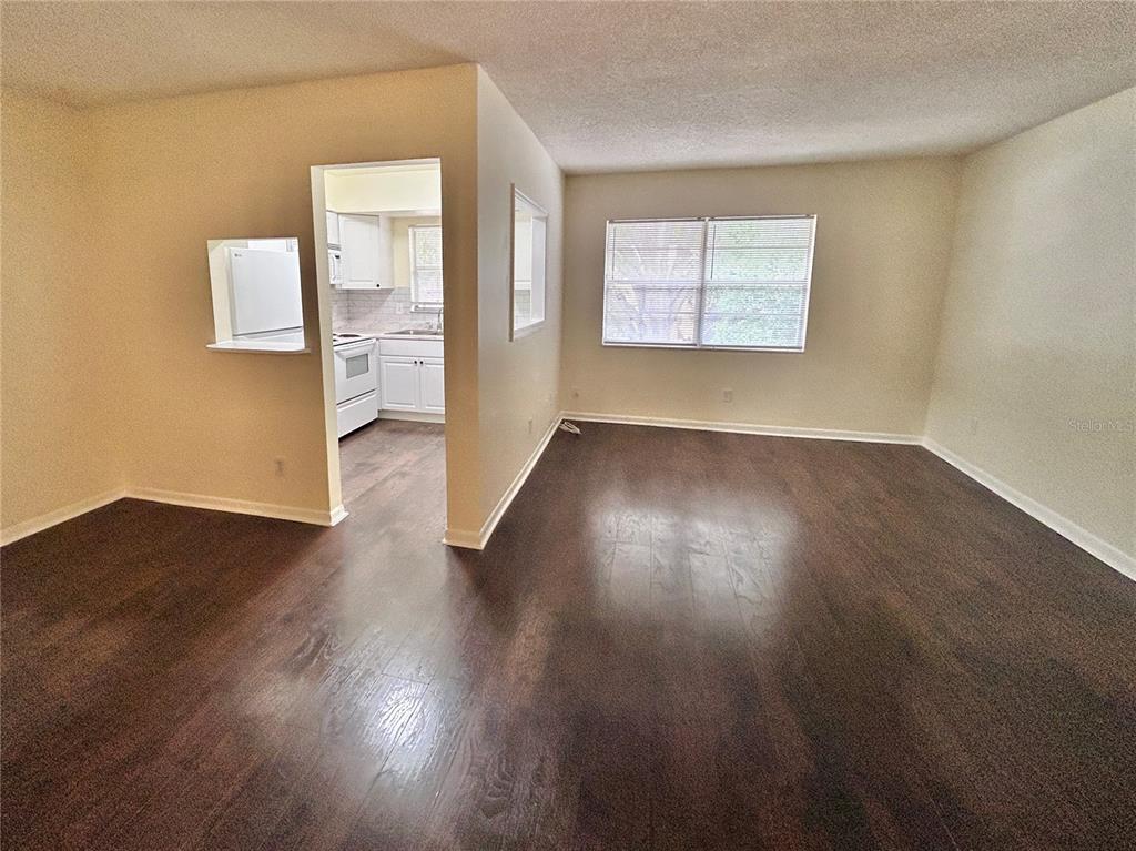 A living room with dark wood-look flooring connects to a kitchen through a doorway — 4455 38TH TERRACE N UNIT B16, ST PETERSBURG, FL