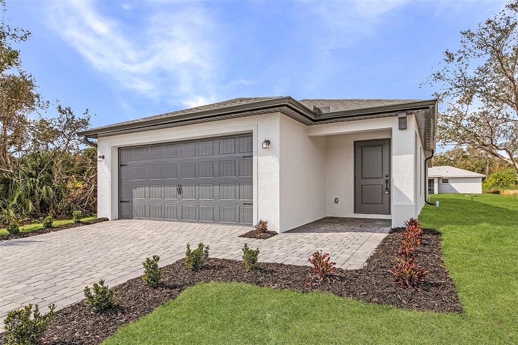 A single-story house exterior with a gray garage door, white stucco walls, and paved driveway — 4743 MICHALER STREET, NORTH PORT, FL