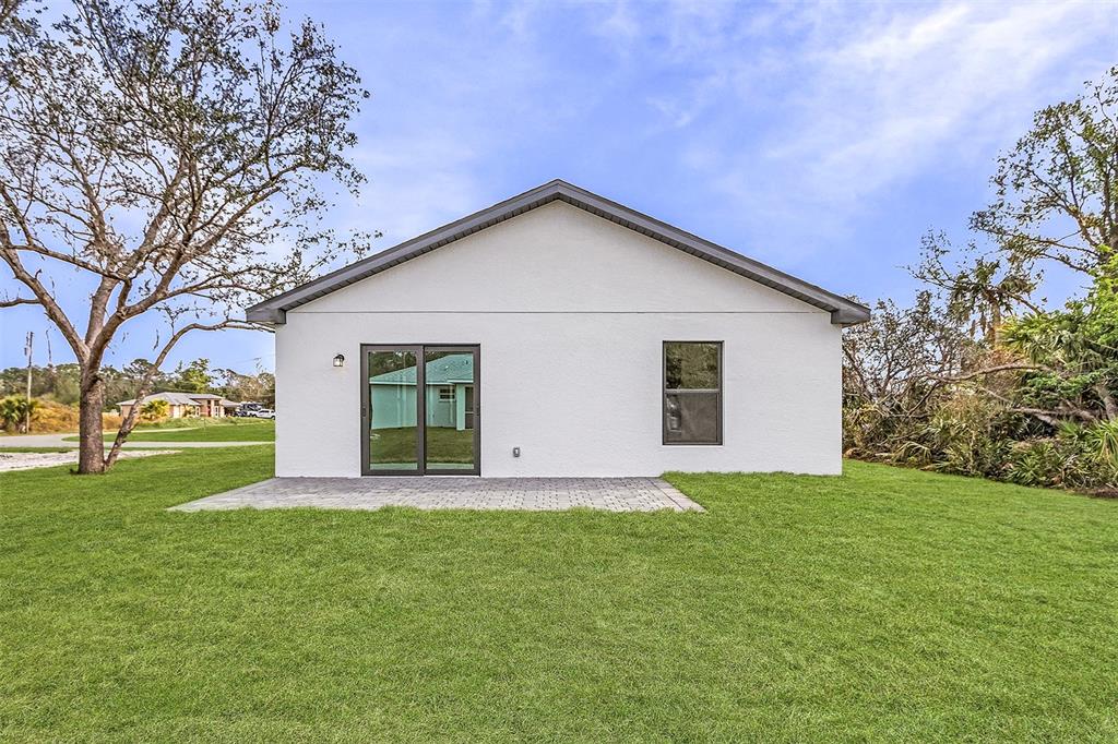 The rear exterior of a white house features a sliding glass door and a patio — 4743 MICHALER STREET, NORTH PORT, FL