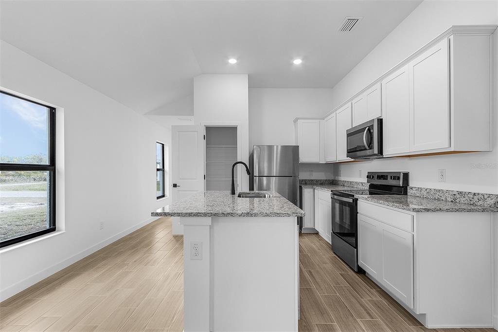 A modern kitchen features white cabinets, granite countertops, stainless steel appliances, and wood-look tile flooring — 4743 MICHALER STREET, NORTH PORT, FL