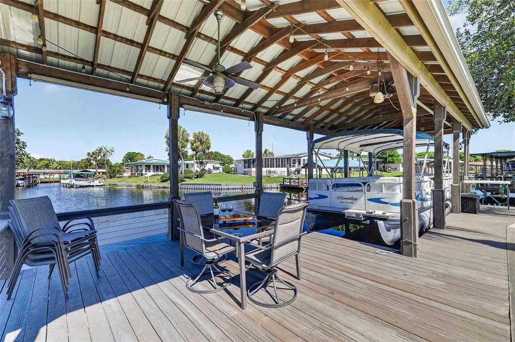 A covered wooden boat dock features a dining set, a pontoon boat, and waterfront views — 1015 SOUTHLAND DRIVE, TAVARES, FL