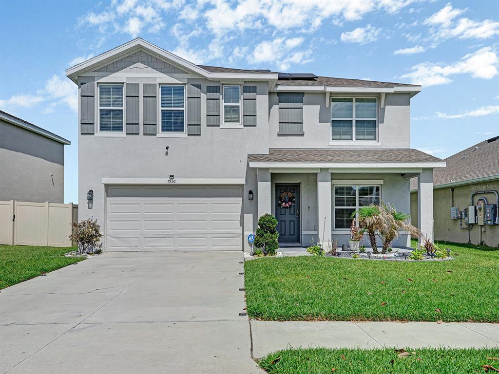 A two-story suburban house features a gray stucco exterior, a two-car garage, and a lawn — 7850 SAIL CLOVER LANE, ZEPHYRHILLS, FL