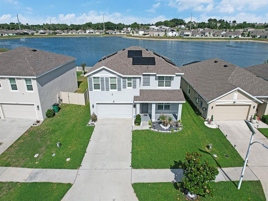An aerial view shows a two-story house with solar panels on the roof near a lake — 7850 SAIL CLOVER LANE, ZEPHYRHILLS, FL
