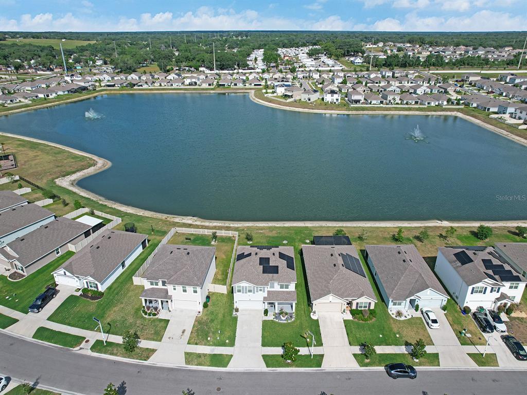 An aerial view shows a row of suburban houses bordering a large community lake — 7850 SAIL CLOVER LANE, ZEPHYRHILLS, FL