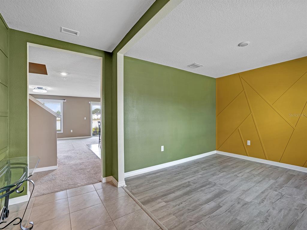 A room with gray wood-look flooring, a green wall, and a gold geometric accent wall — 7850 SAIL CLOVER LANE, ZEPHYRHILLS, FL