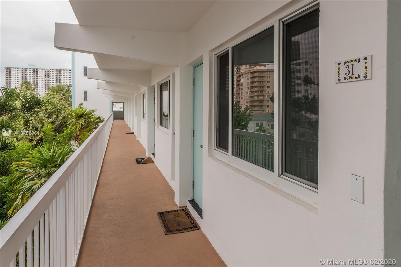 An exterior walkway with a white railing overlooks tropical plants and nearby apartment buildings — 1801 S Surf Road # 2C, Hollywood FL 33019, HOLLYWOOD, FL