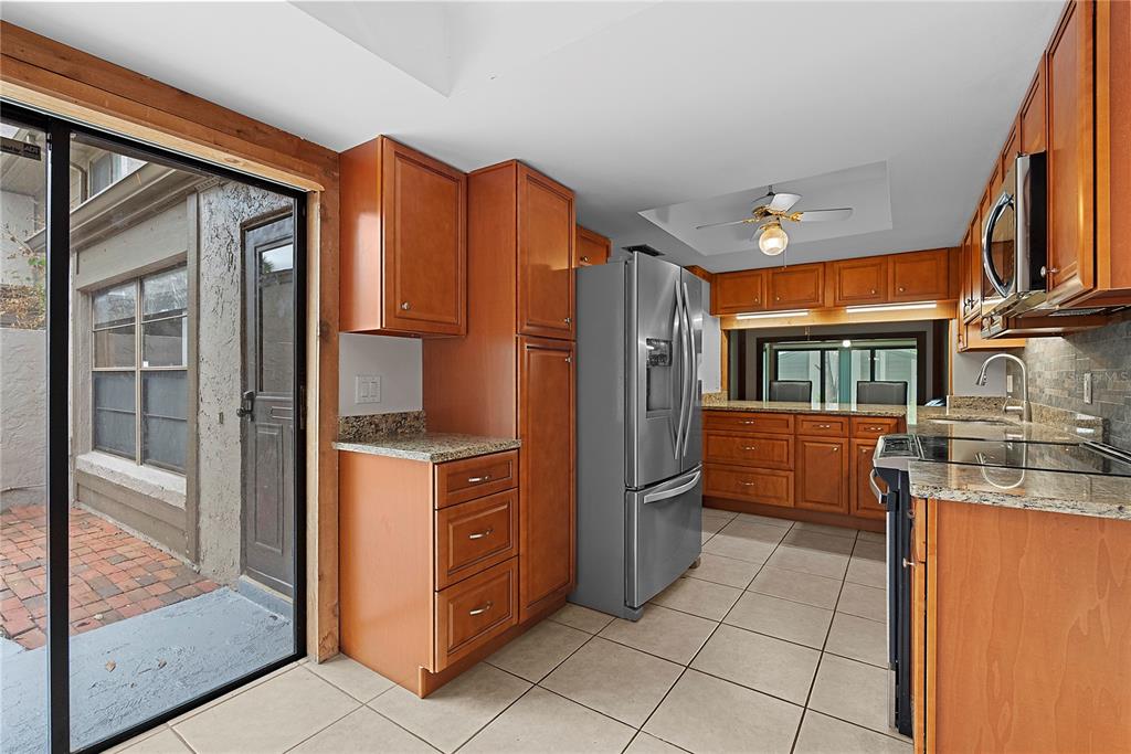 A kitchen with wood cabinets, granite countertops, stainless steel appliances, and a sliding glass door — 497 MEADOWOOD BOULEVARD, FERN PARK, FL
