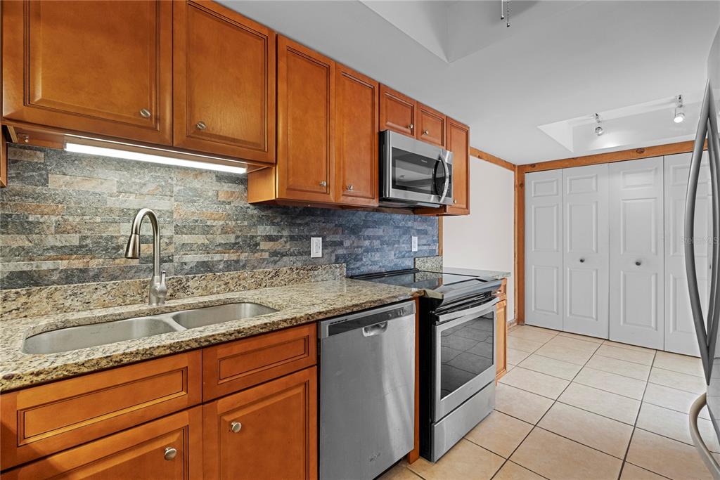 A kitchen features wood cabinets, granite countertops, stainless steel appliances, and a stone tile backsplash — 497 MEADOWOOD BOULEVARD, FERN PARK, FL