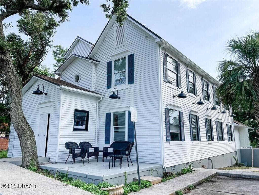 A two-story white house with blue shutters and a small patio with outdoor furniture — 404 S RIDGEWOOD AVENUE, DAYTONA BEACH, FL