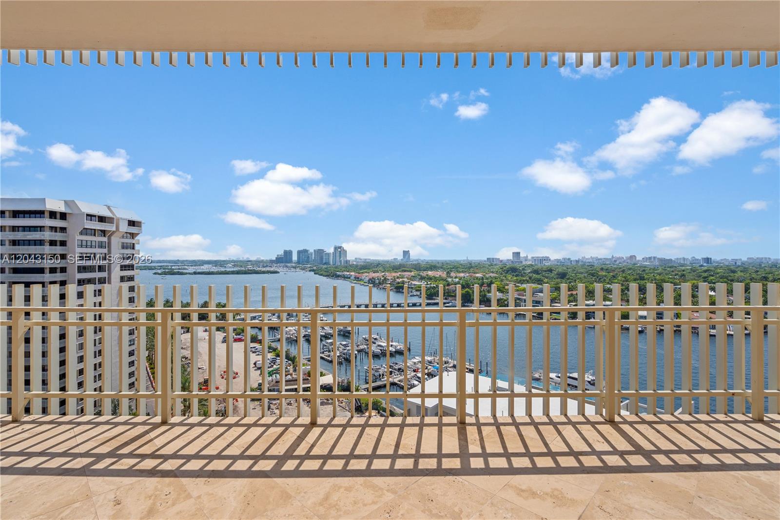 A balcony with a beige tiled floor overlooks a marina and a distant city skyline — 3 Grove Isle Dr # C1610, Miami FL 33133, MIAMI, FL