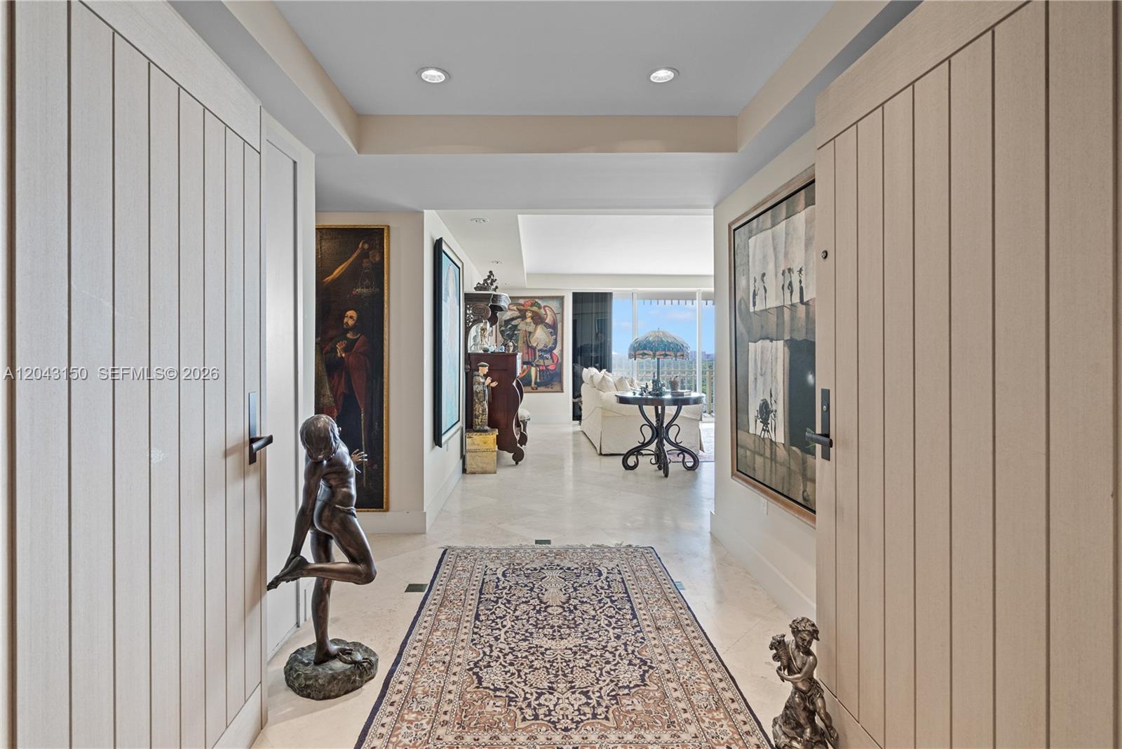 A hallway with light wood doors, art, and a rug leads to a living area — 3 Grove Isle Dr # C1610, Miami FL 33133, MIAMI, FL