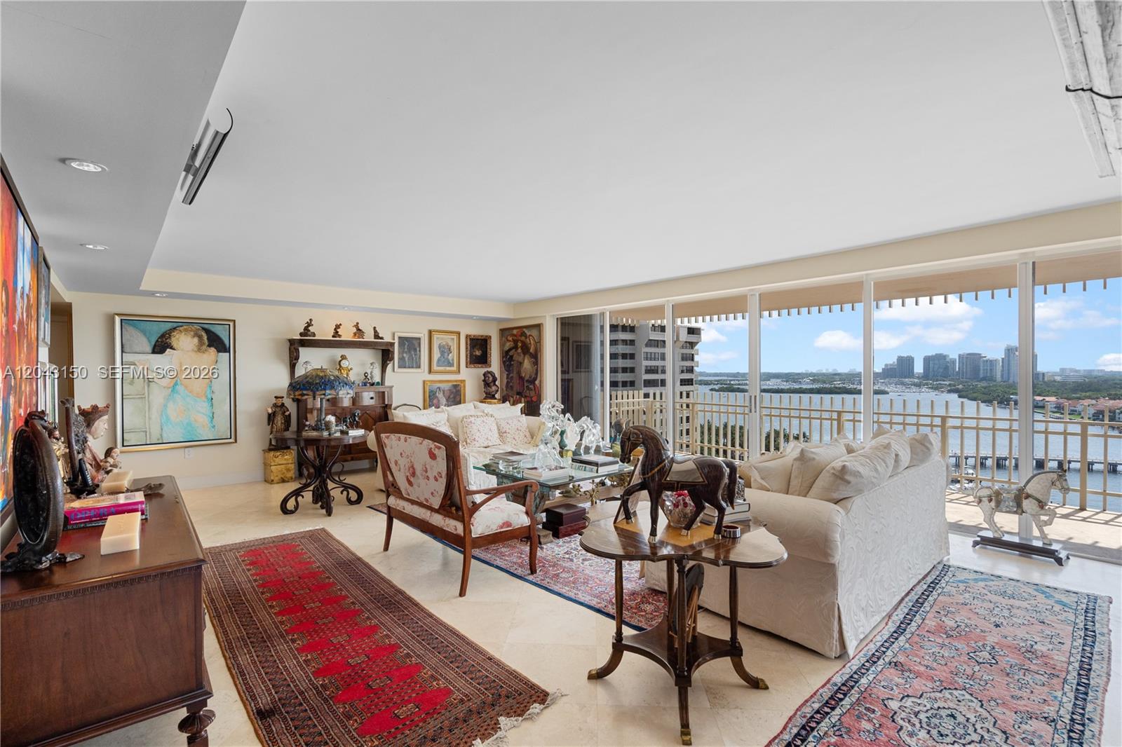 A living room features traditional furniture, area rugs, and floor-to-ceiling windows overlooking a bay — 3 Grove Isle Dr # C1610, Miami FL 33133, MIAMI, FL