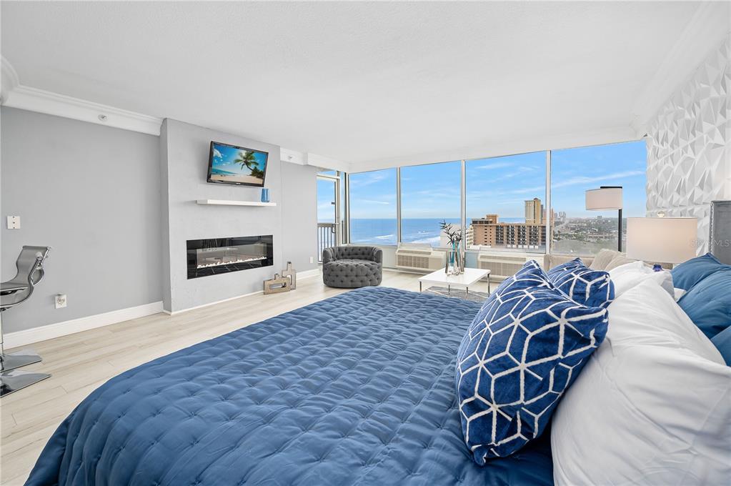 A bedroom with a blue quilted bed, fireplace, and floor-to-ceiling windows overlooking the ocean — 2700 N ATLANTIC AVENUE UNIT 1201, DAYTONA BEACH, FL