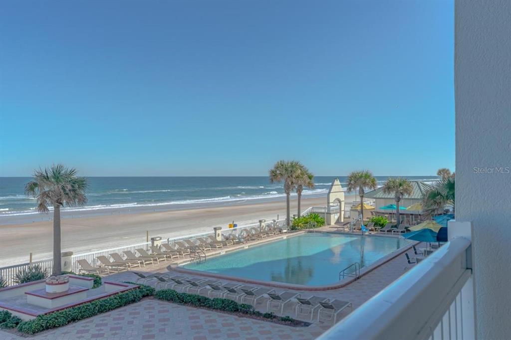 An elevated view of a swimming pool and lounge chairs overlooking a sandy beach — 2700 N ATLANTIC AVENUE UNIT 1201, DAYTONA BEACH, FL