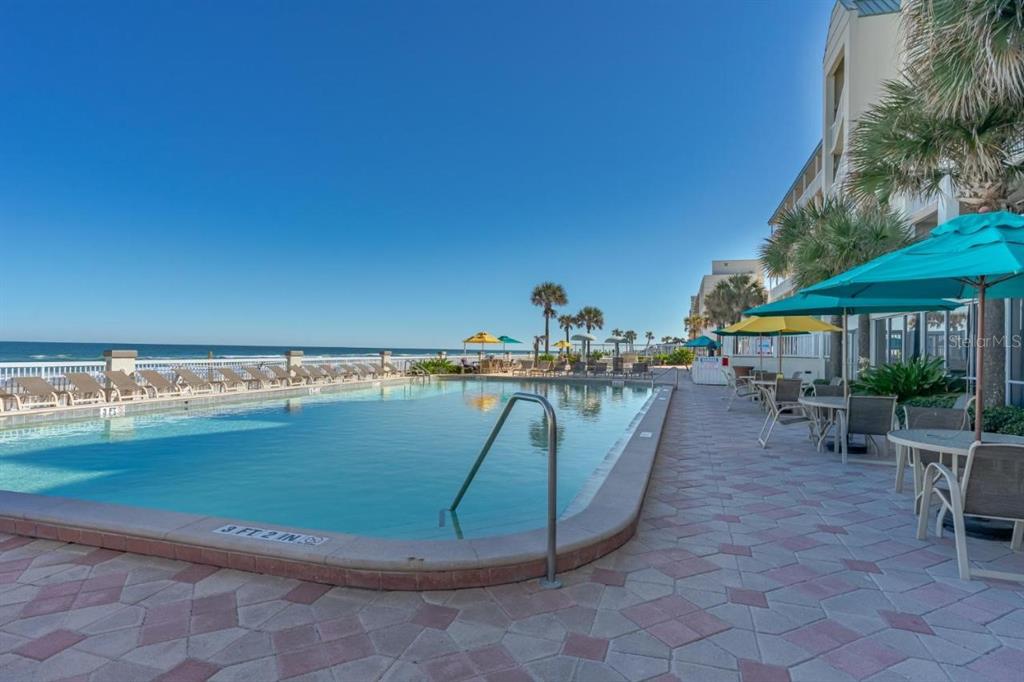 An outdoor swimming pool with lounge chairs and umbrellas overlooks the ocean next to a building — 2700 N ATLANTIC AVENUE UNIT 1201, DAYTONA BEACH, FL