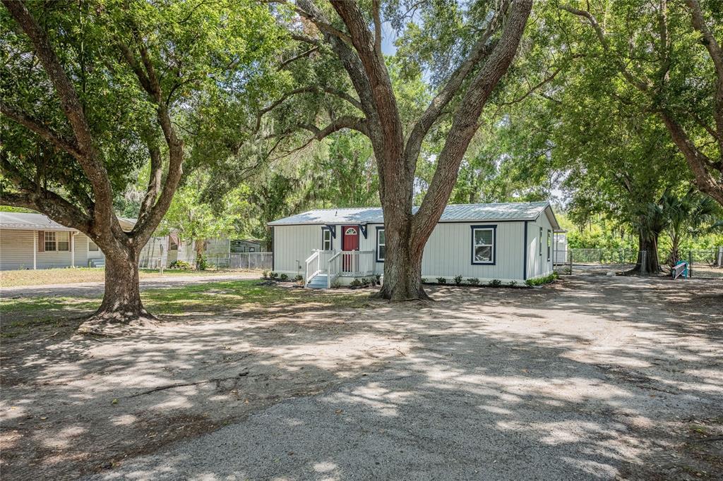 A light-colored mobile home sits on a dirt lot shaded by large oak trees — 5220 SPRING CREEK DR, LAKELAND, FL