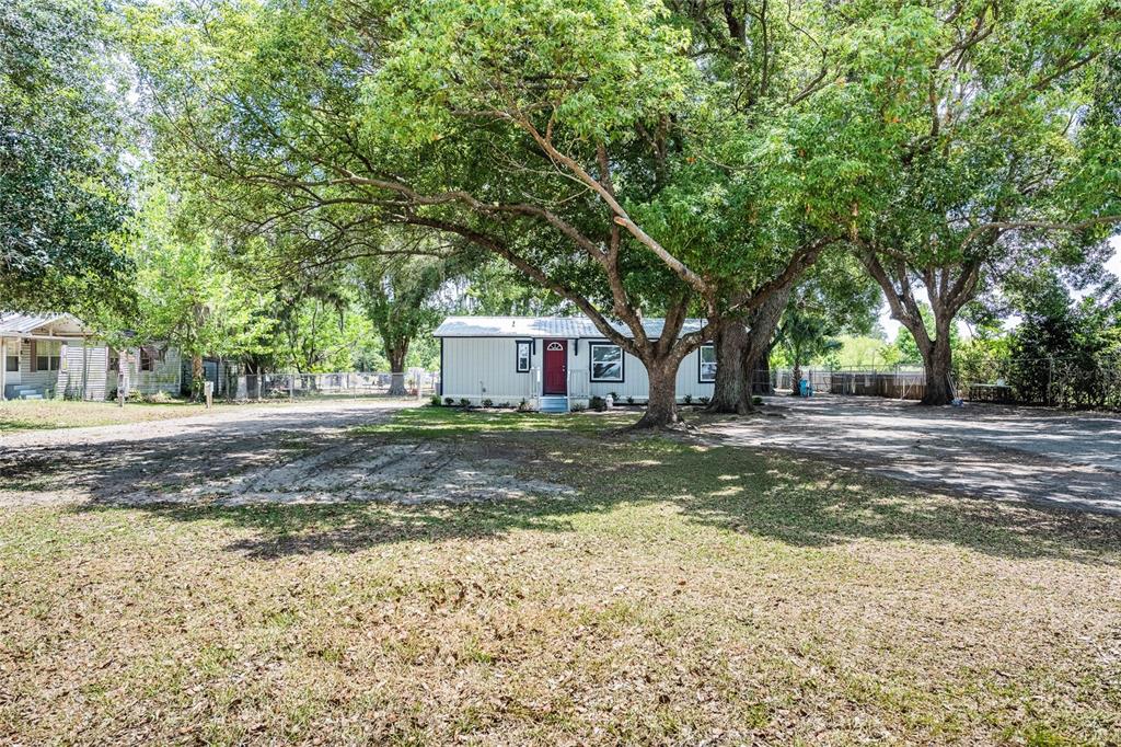 A single-story manufactured home with a red door sits under large trees on a lot — 5220 SPRING CREEK DR, LAKELAND, FL