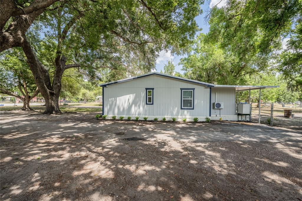 A light-colored manufactured home sits on a dirt lot shaded by large oak trees — 5220 SPRING CREEK DR, LAKELAND, FL