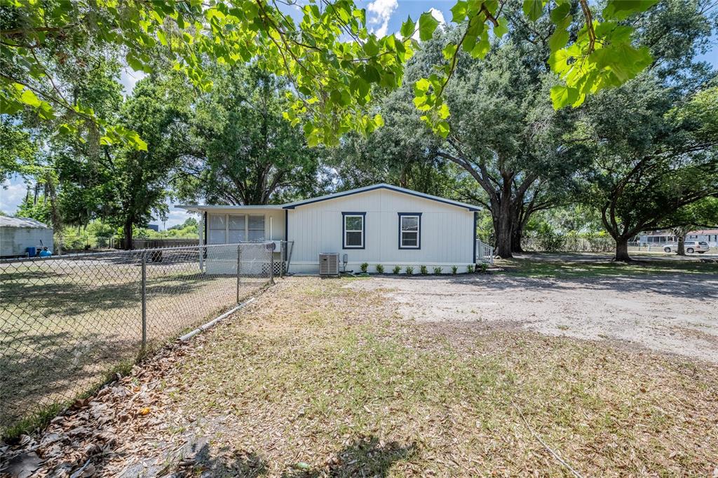 A single-story manufactured home with light siding stands on a dirt lot with trees — 5220 SPRING CREEK DR, LAKELAND, FL
